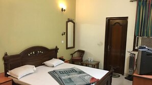 Une chambre à coucher avec un lit en bois, une table de chevet, une chaise, un bureau avec un ordinateur, un miroir et une porte.