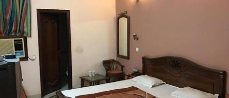 A hotel room with a bed, a desk, a chair, a mirror, and a wall-mounted light.