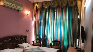 Une chambre d’hôtel avec un lit, un bureau, une chaise, une télévision et une fenêtre agrémentée de rideaux colorés.