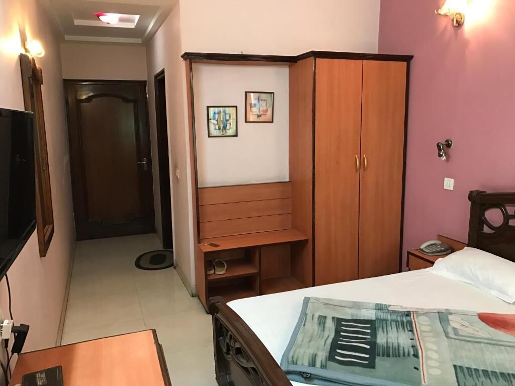 A hotel room with a bed, a wooden wardrobe, a desk, and a wall-mounted TV.