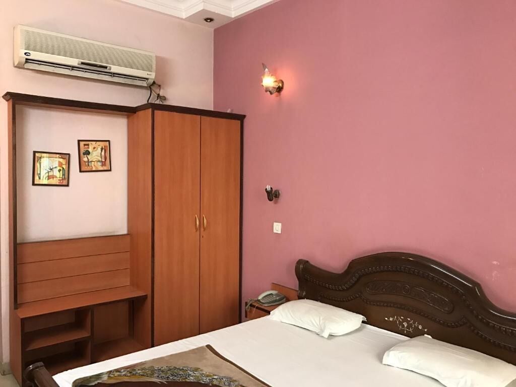 A bedroom with a bed, a wardrobe, a bedside table with a lamp, and an air conditioning unit.