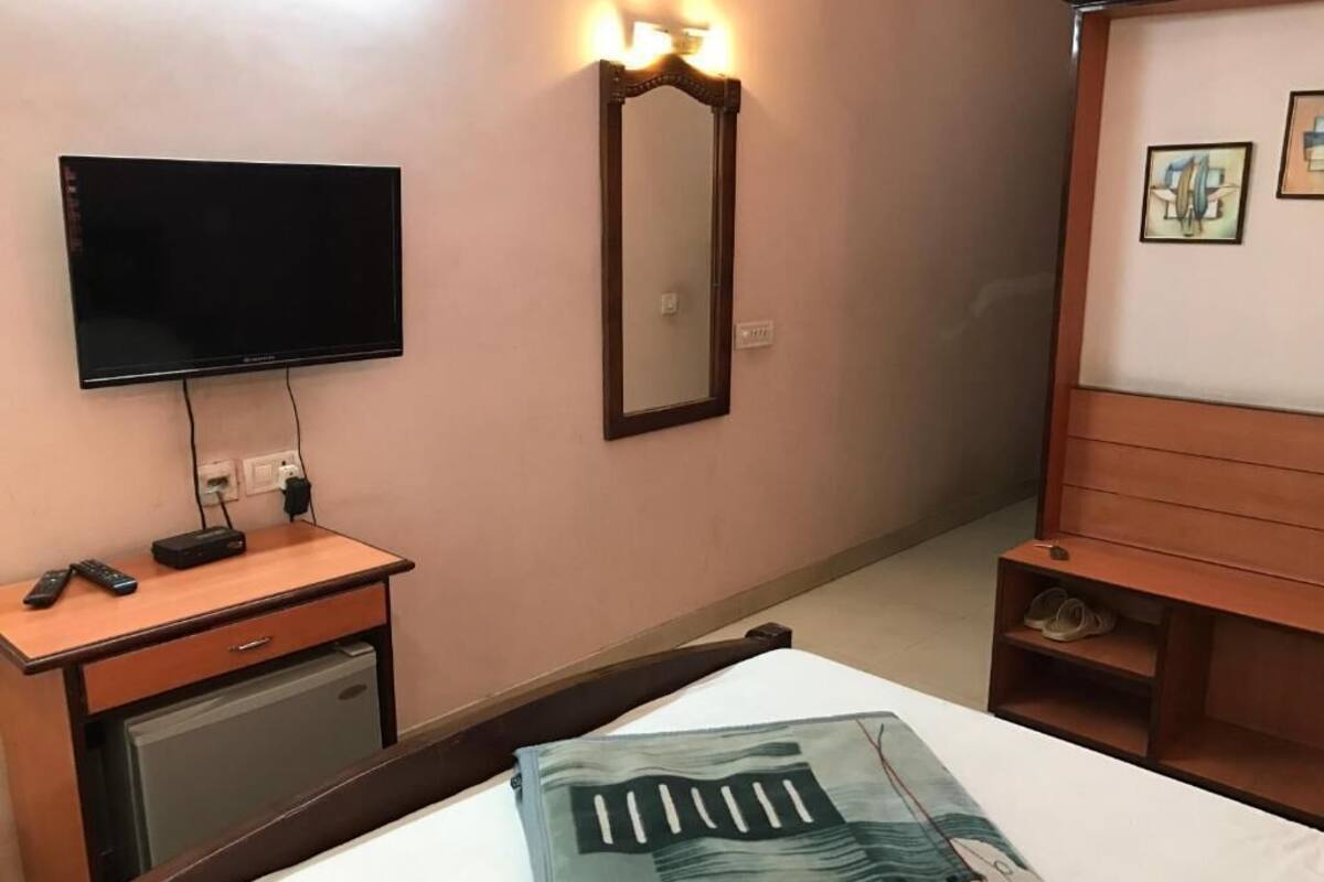 Una camera d'albergo con una televisione, uno specchio, una scrivania con un telecomando, un letto con una coperta e una testiera in legno.