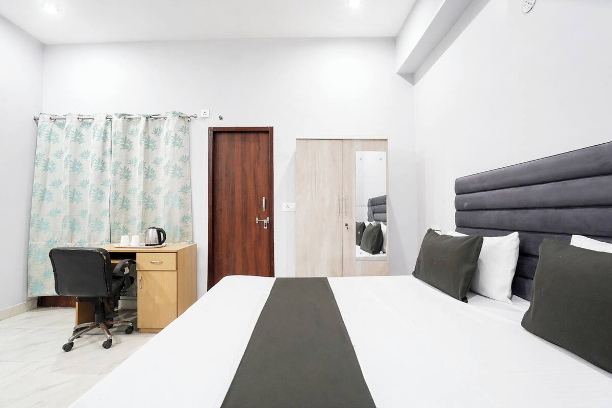 Quarto de hotel com uma cama, uma escrivaninha com cadeira, um guarda-roupa de madeira e um espelho.