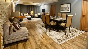A spacious living room with a dining area, wooden flooring, and a large window. - Centaurus Ultra Luxury Apartments (Islamabad)
