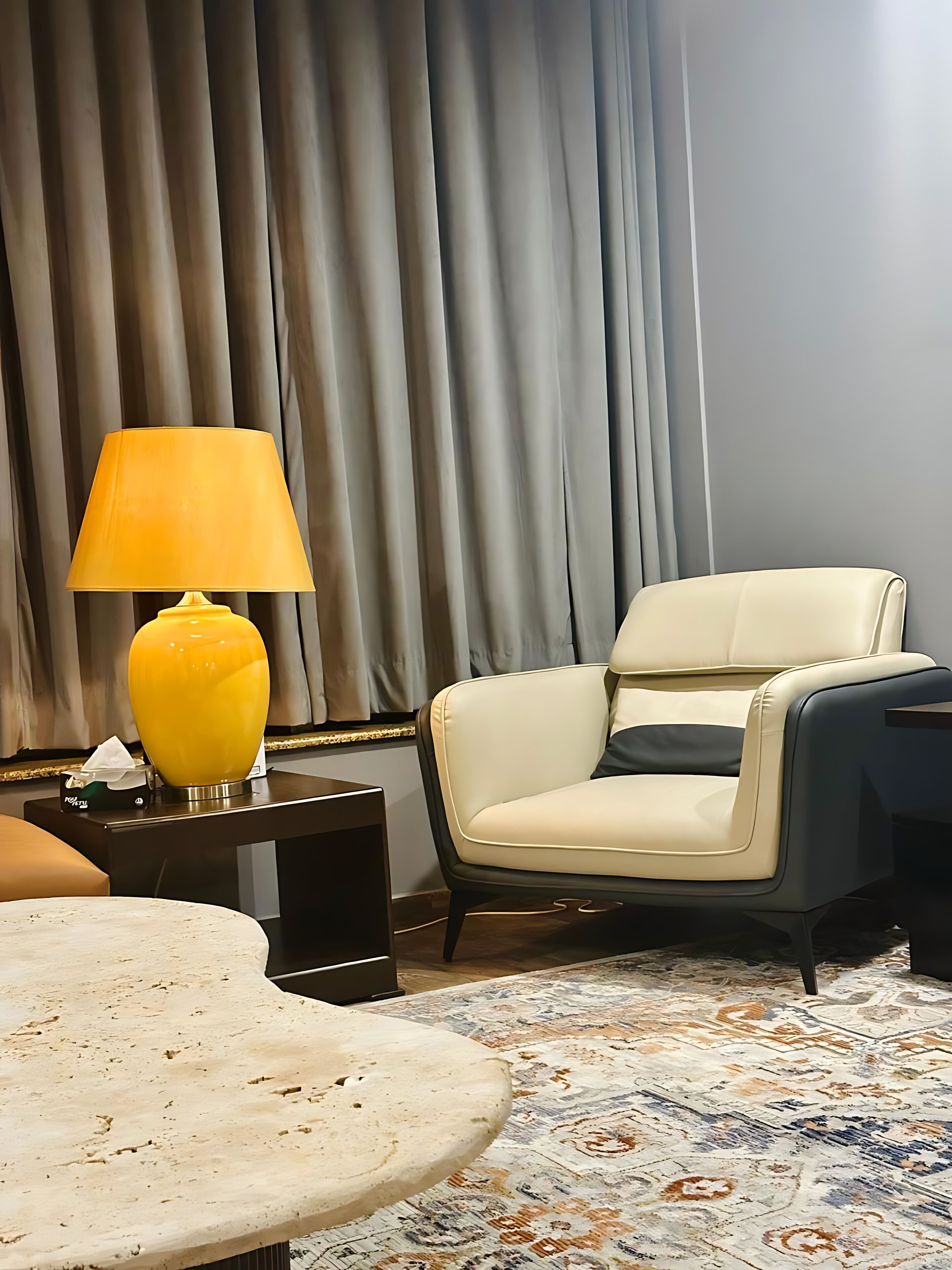 A hotel room with a round table, a yellow lamp, a white chair, and a patterned carpet.