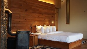 A wooden-paneled room with a bed, a nightstand, a lamp, and a fireplace. - Mountain Resort (Jakar)