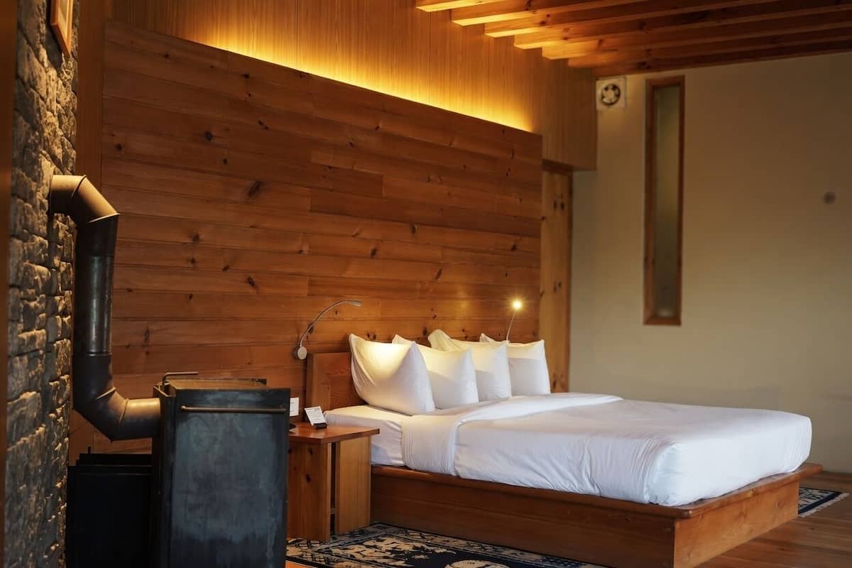 Una habitación con paneles de madera, una cama, una mesita de noche, una lámpara y una chimenea.