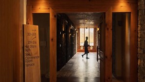 A wooden corridor with a sign indicating room numbers and amenities like a hot stone bath, spa, conference room, and terrace. - Mountain Resort (Jakar)
