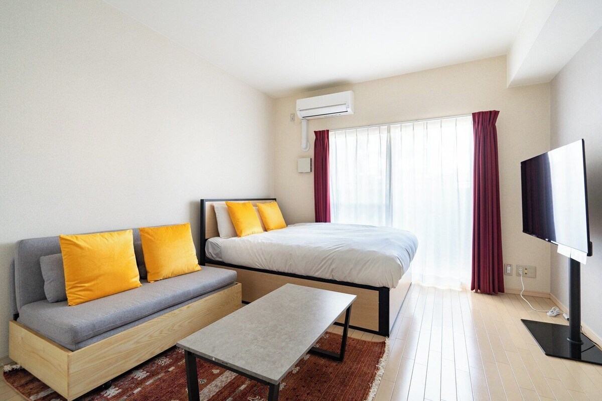 A modern hotel room with a sofa, bed, flat-screen TV, and an air conditioning unit.
