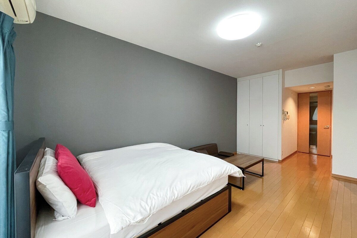A bedroom with a bed, a desk, a wardrobe, and a door leading to another room.