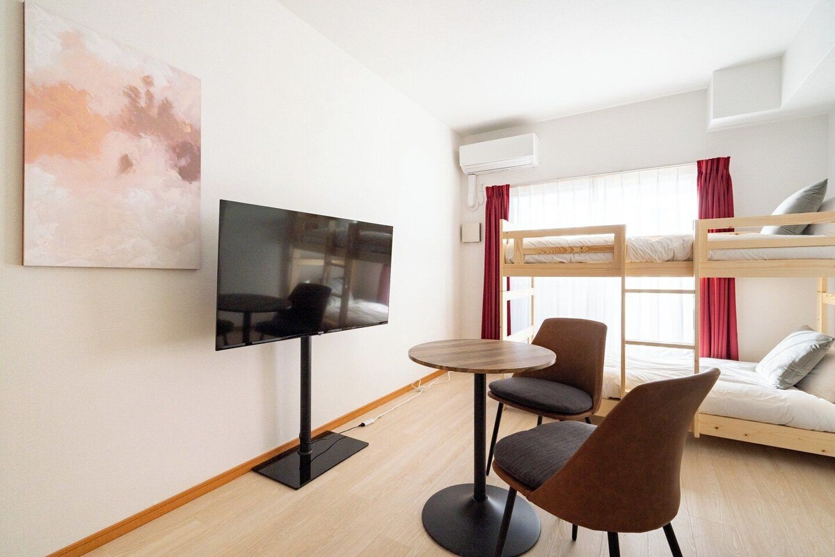 A room with a TV, bunk beds, a table, and chairs.