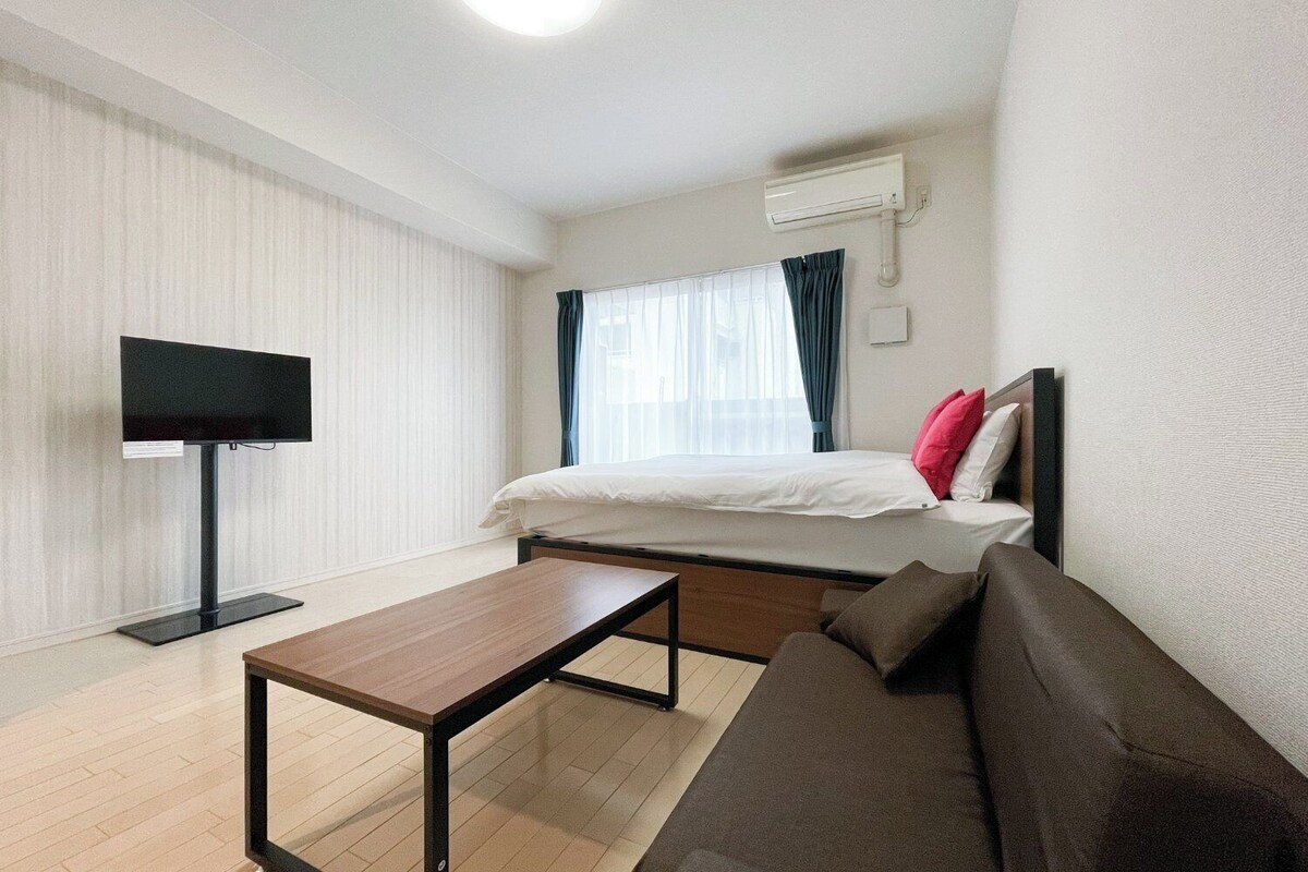 A hotel room with a bed, a TV, a sofa, and a wooden table.