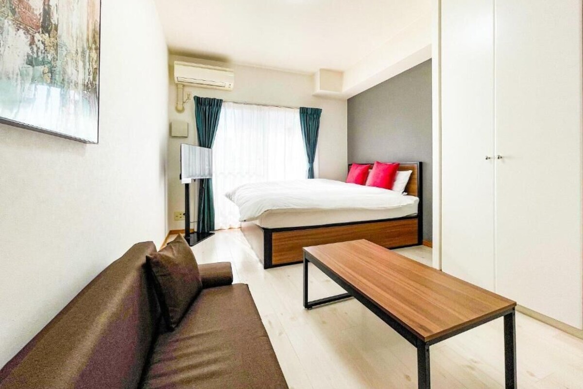 A modern hotel room with a bed, a wooden table, a sofa, and a painting on the wall.