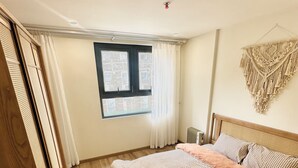 A bedroom with a bed, wooden flooring, a window with curtains, and a macrame wall hanging. - Boho and Cozy Home in Sapa -5Min to Center (Sapa)