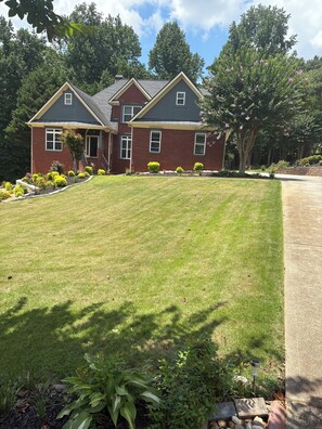 A two-story house with a well-maintained lawn, a driveway, and a garden with various plants.