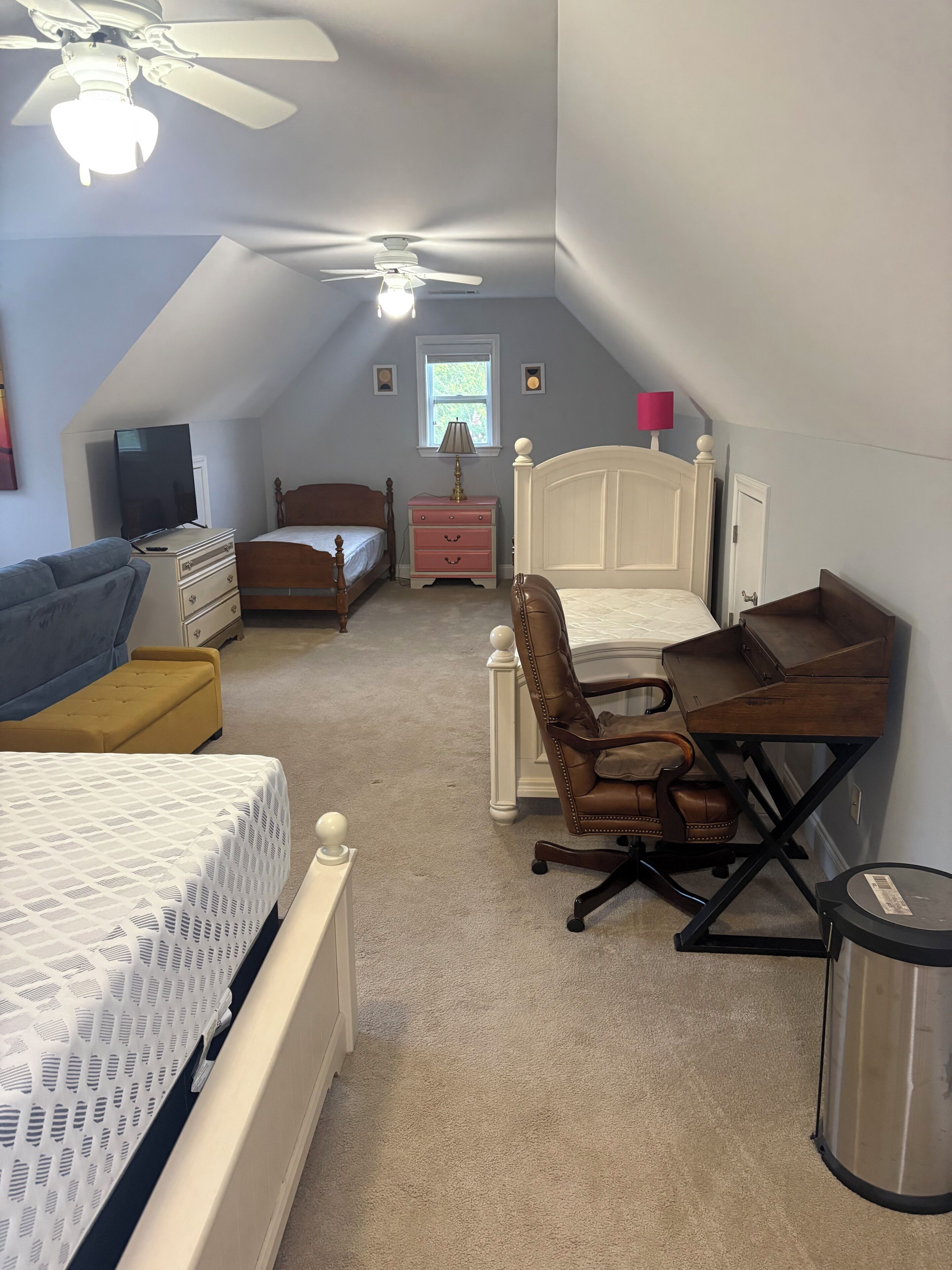 Un dormitorio con cama, escritorio, silla y ventilador de techo.
