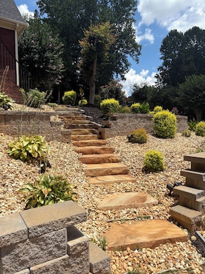 A stone staircase leading up to a building, surrounded by a landscaped garden with various plants and trees.