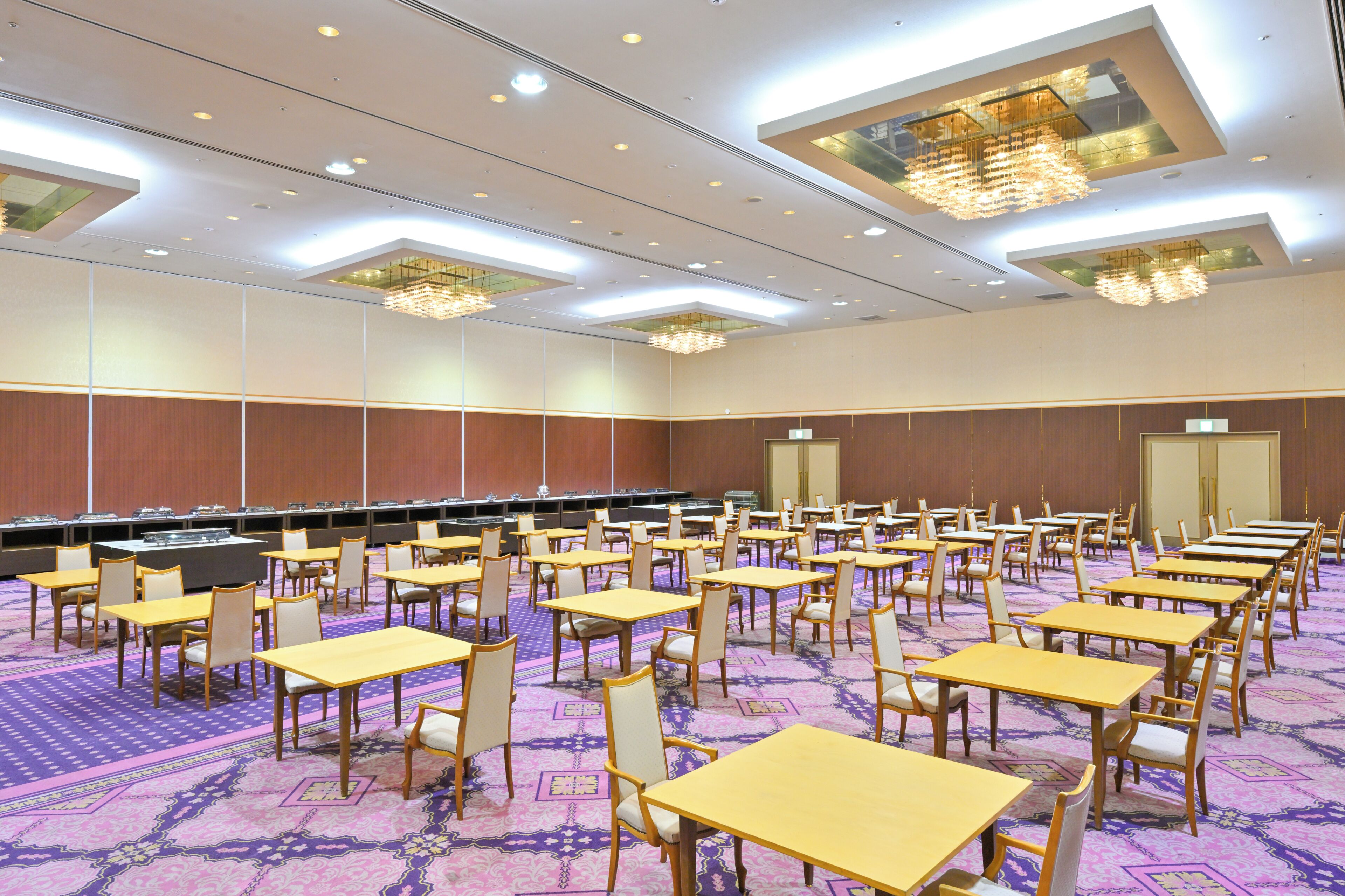 A conference room with multiple tables and chairs, a carpeted floor, and a ceiling with recessed lighting and chandeliers.