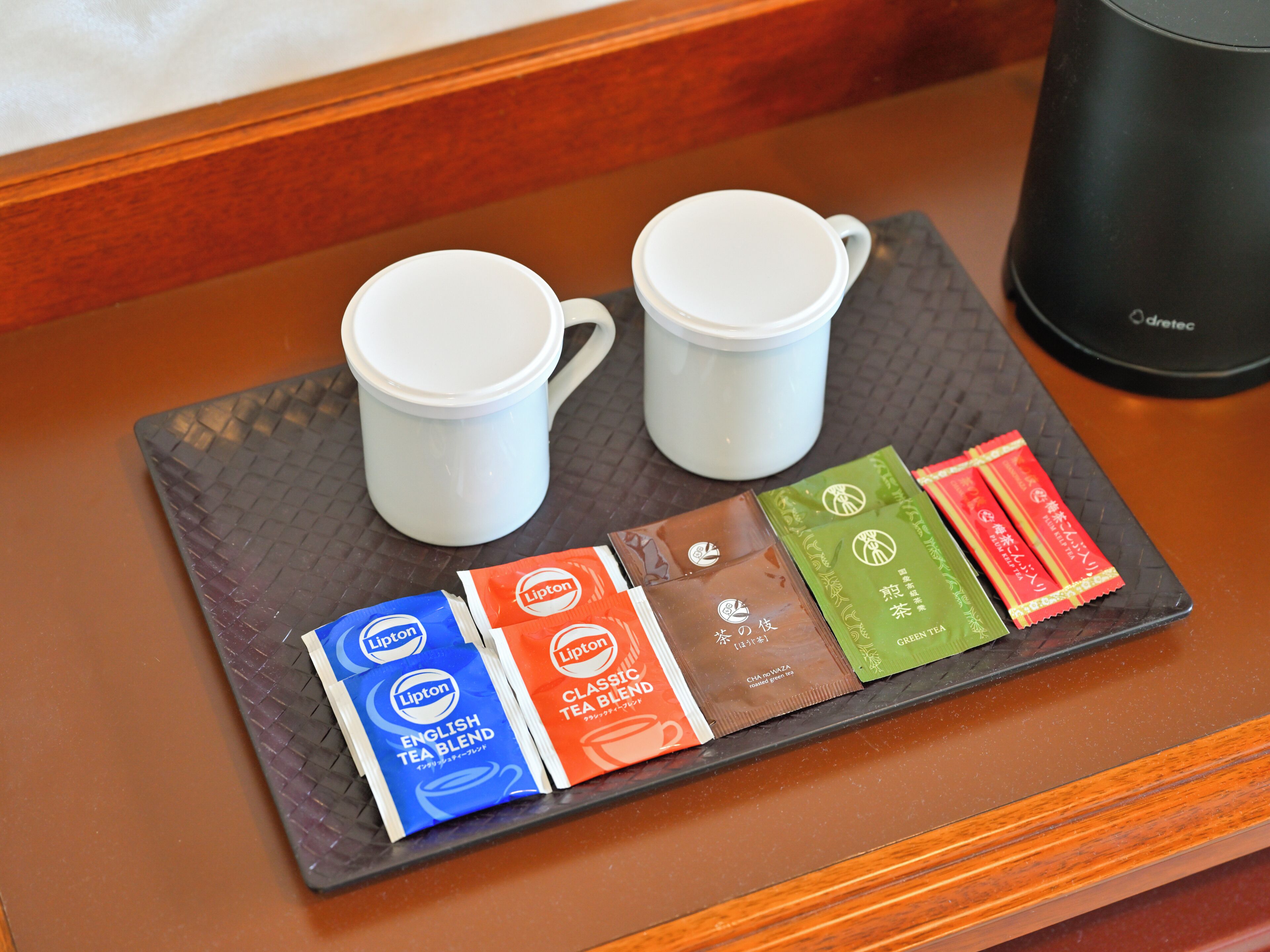 A tray with two white cups and tea packets on a wooden surface.