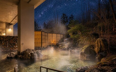 A hot spring area with a stone wall, wooden structure, and a starry night sky.