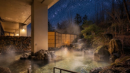 A hot spring area with a stone wall, wooden structure, and a starry night sky.