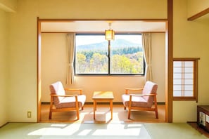 A traditional Japanese room with tatami flooring, a low table, two chairs, a window with a view of mountains, and a sliding door. - Livemax Resort Hachimantai (Hachimantai)