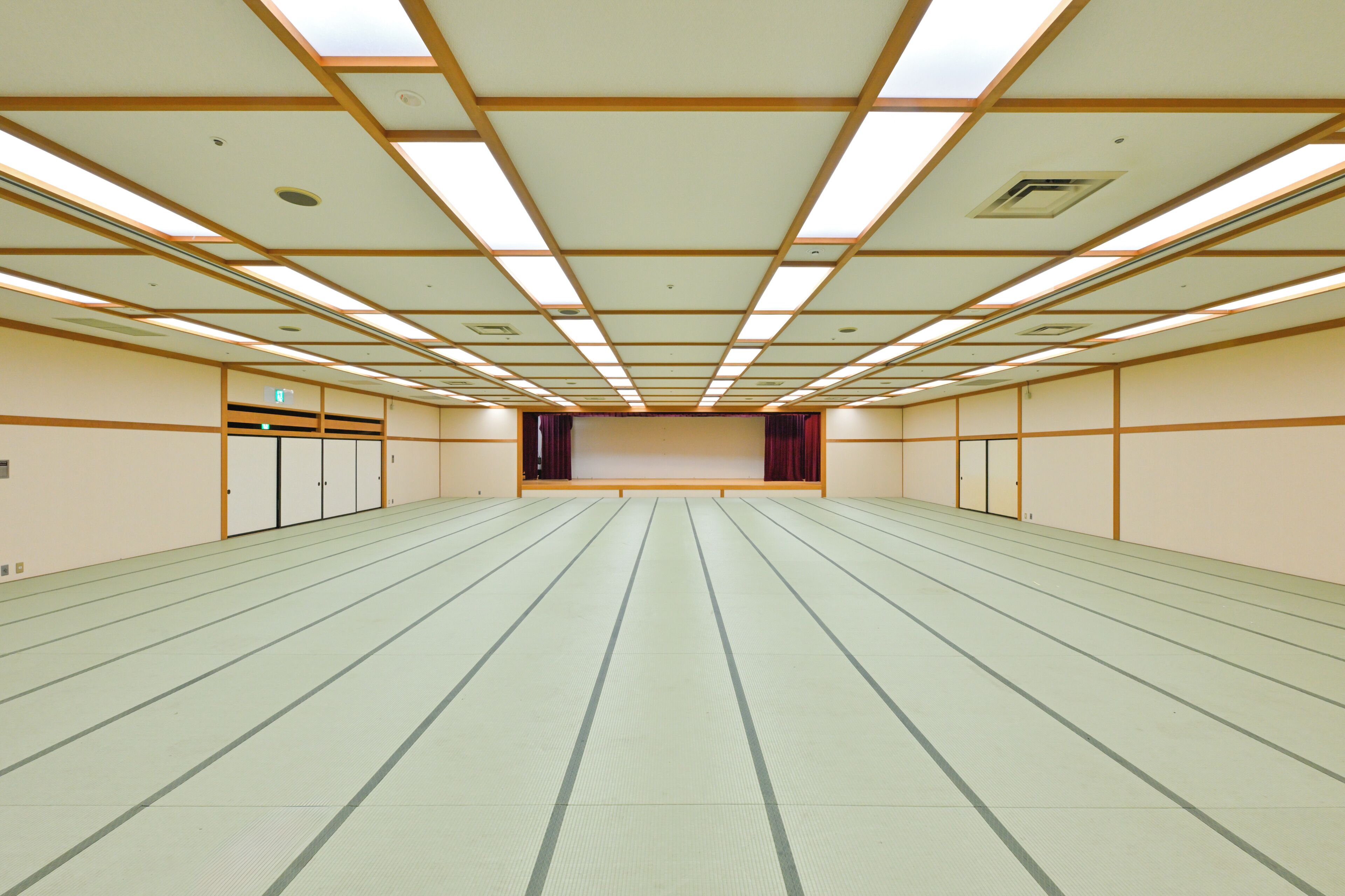 Una habitación amplia y vacía con suelo de esteras de tatami, paneles de madera en las paredes e iluminación fluorescente en el techo.