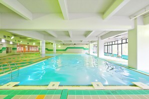 Una piscina interior con carriles de natación, un trampolín y una zona de estar con sillas.