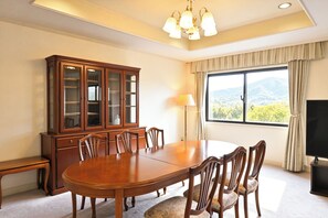 Un salón de conferencias con una gran mesa de madera, sillas, un armario, una lámpara y un televisor.