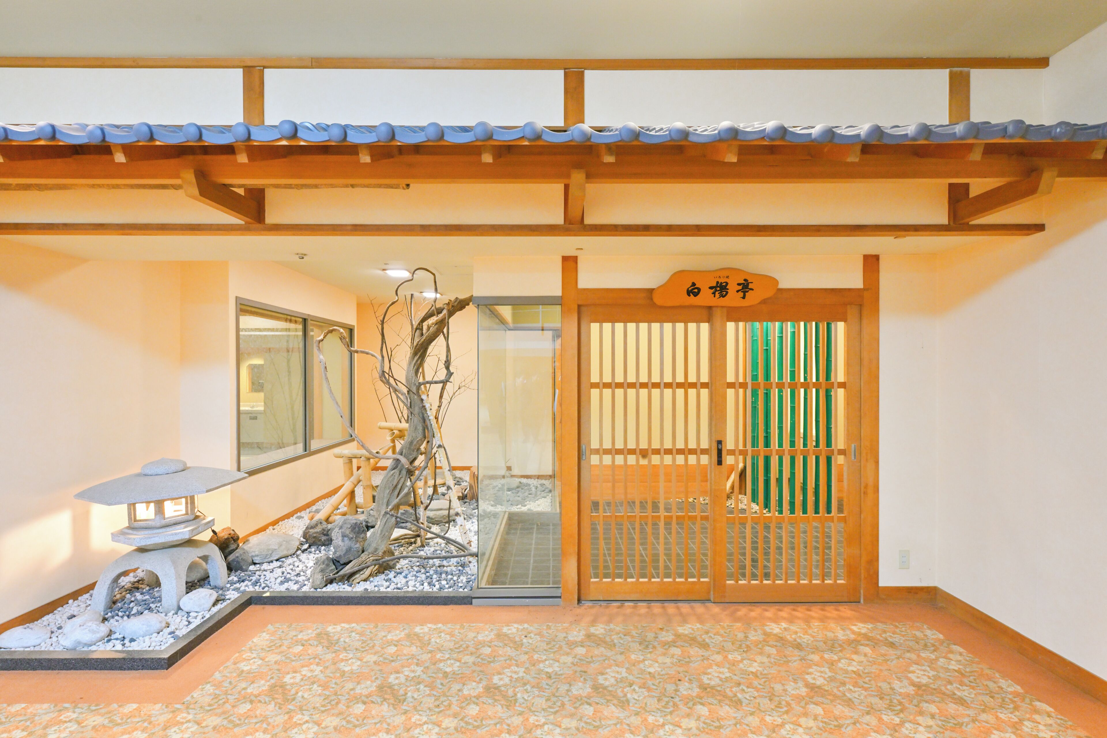 Une entrée de style japonais traditionnel, avec une porte en bois, une lanterne en pierre et un petit arbre.