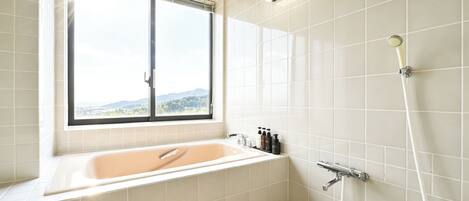 A bathroom with a bathtub, a window, and a shower.