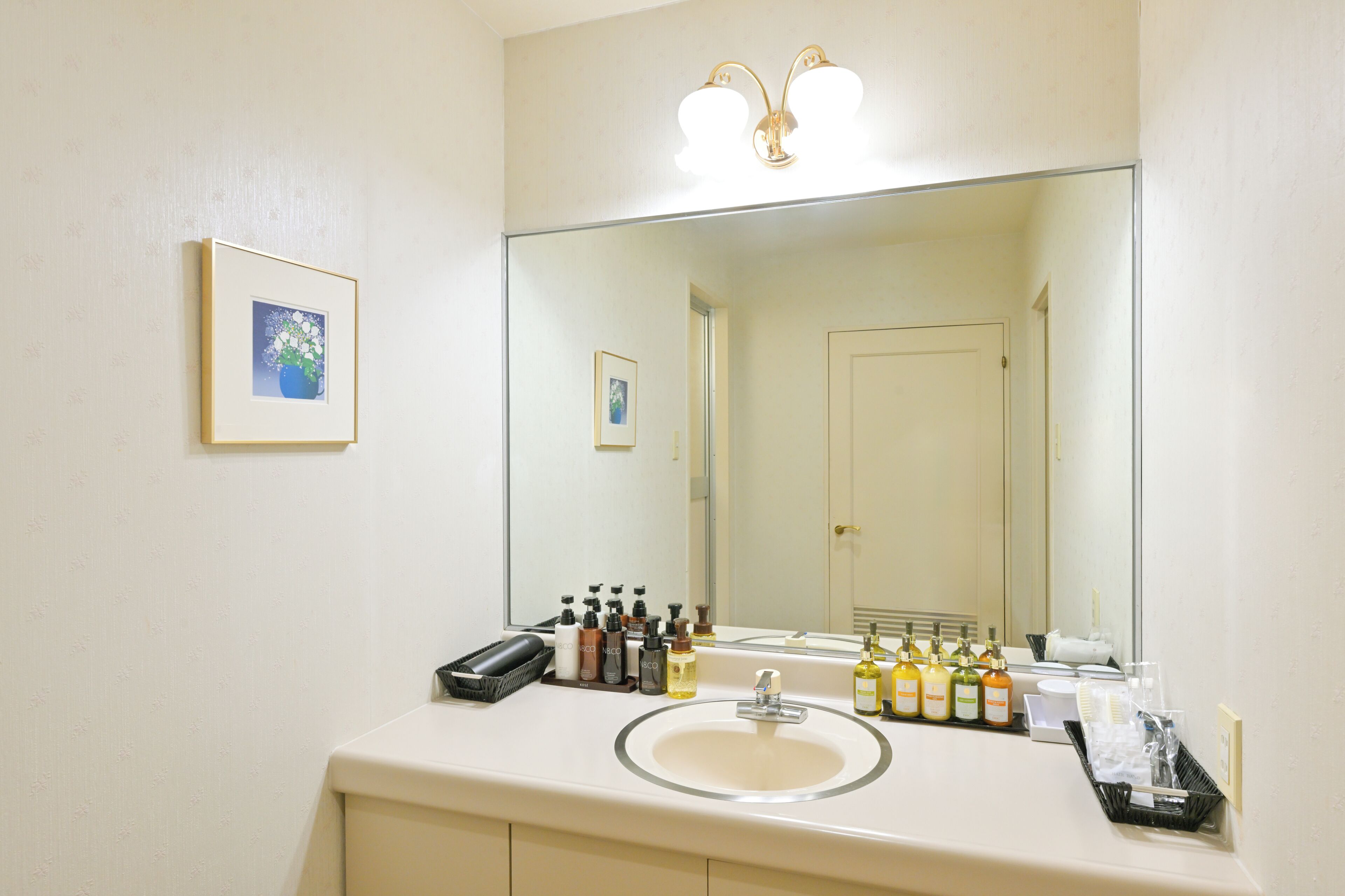 Casa de banho de hotel com um espelho grande, uma pia, artigos de higiene e um quadro emoldurado na parede.