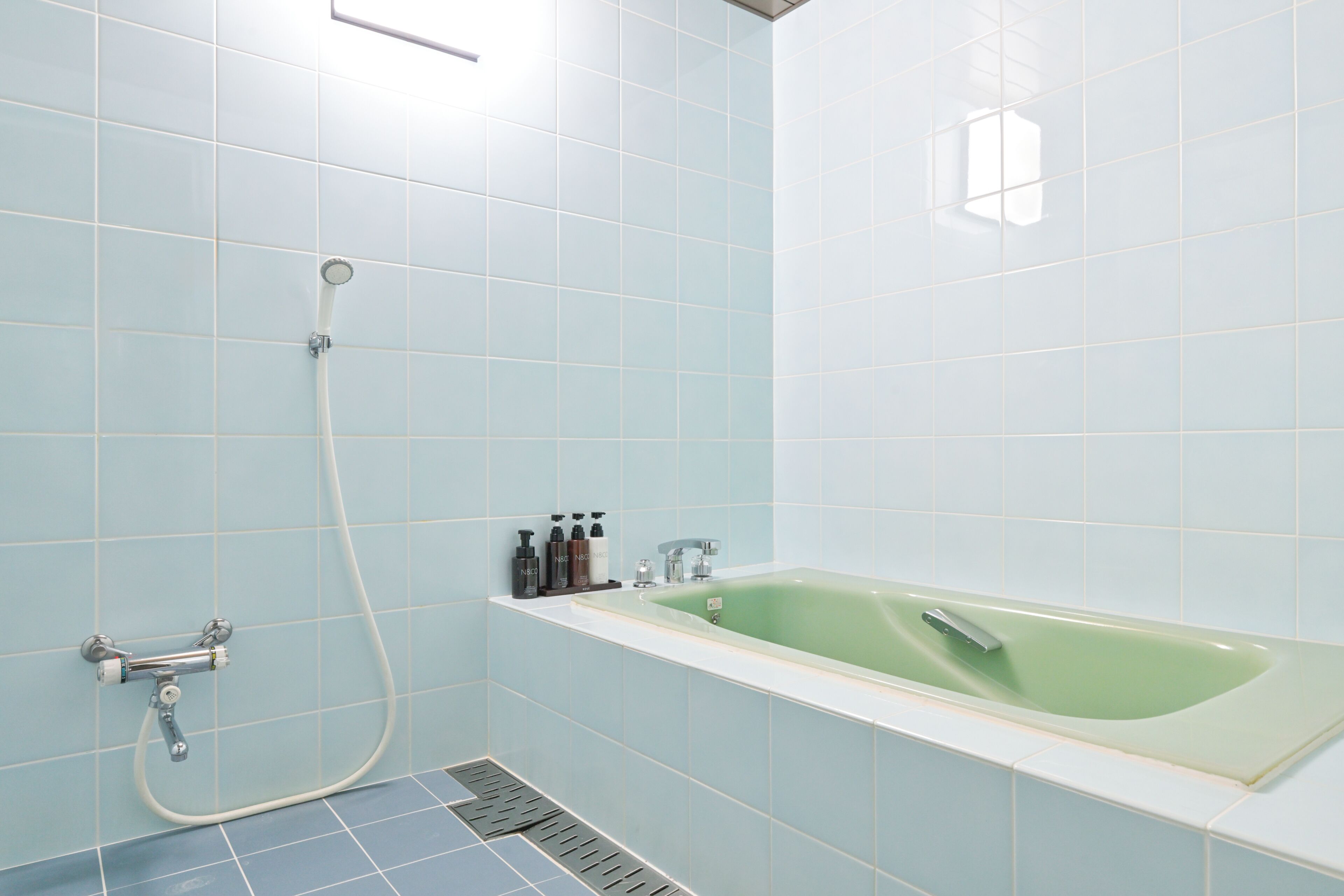 A bathroom with a green bathtub, a shower, and a tiled floor.