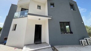 A modern two-story building with a balcony, a door, and two air conditioning units.