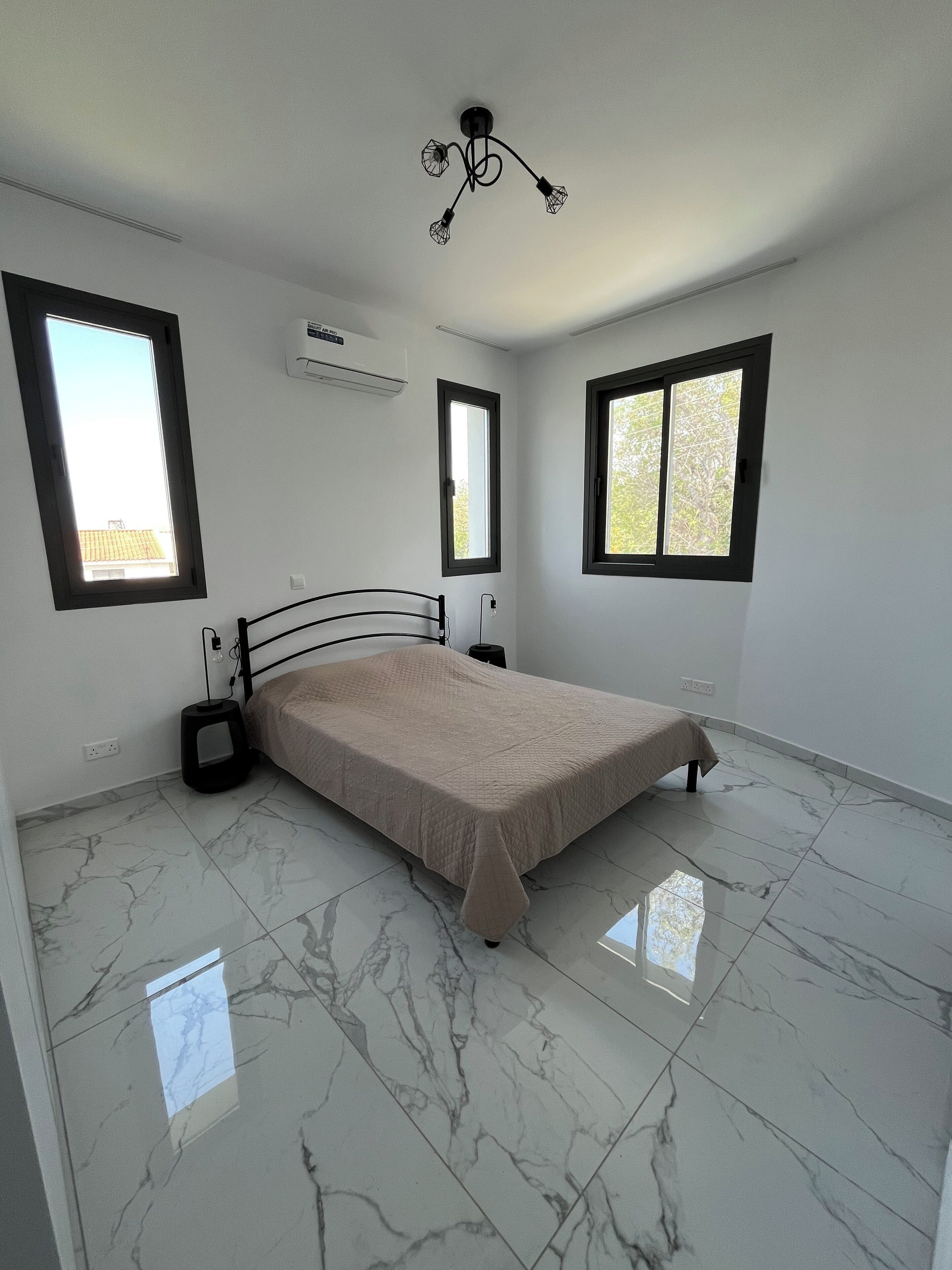 Un dormitorio con cama, dos ventanas, aire acondicionado y piso de mármol.