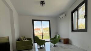 A spacious room with a green sofa, two green chairs, a marble floor, and a large window.
