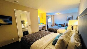 Quarto de hotel com duas camas, uma escrivaninha com cadeira, um espelho e uma televisão na parede.