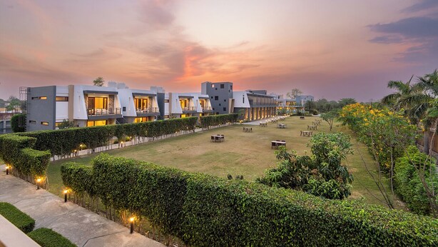 A modern hotel with multiple buildings, a well-maintained lawn, and a sunset sky. - DLS Forest Vines Resort & Spa (Ramnagar)