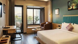 A hotel room with a bed, a desk, a chair, a small table, and a window with a view. - DLS Forest Vines Resort & Spa (Ramnagar)