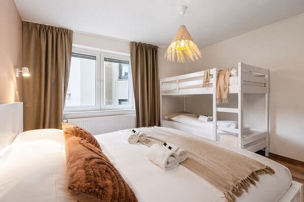 A hotel room with a bed, a window, a bunk bed, and a hanging light fixture. - Raphaelle | Stylish Coastal Apartment in Ostend | Sleeps 8 (Oostende)