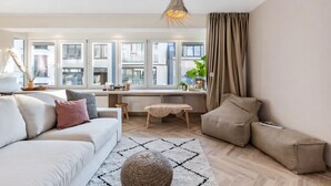 Ein modernes Wohnzimmer mit Sofa, Hocker und einem Essbereich mit Tisch und Stühlen.