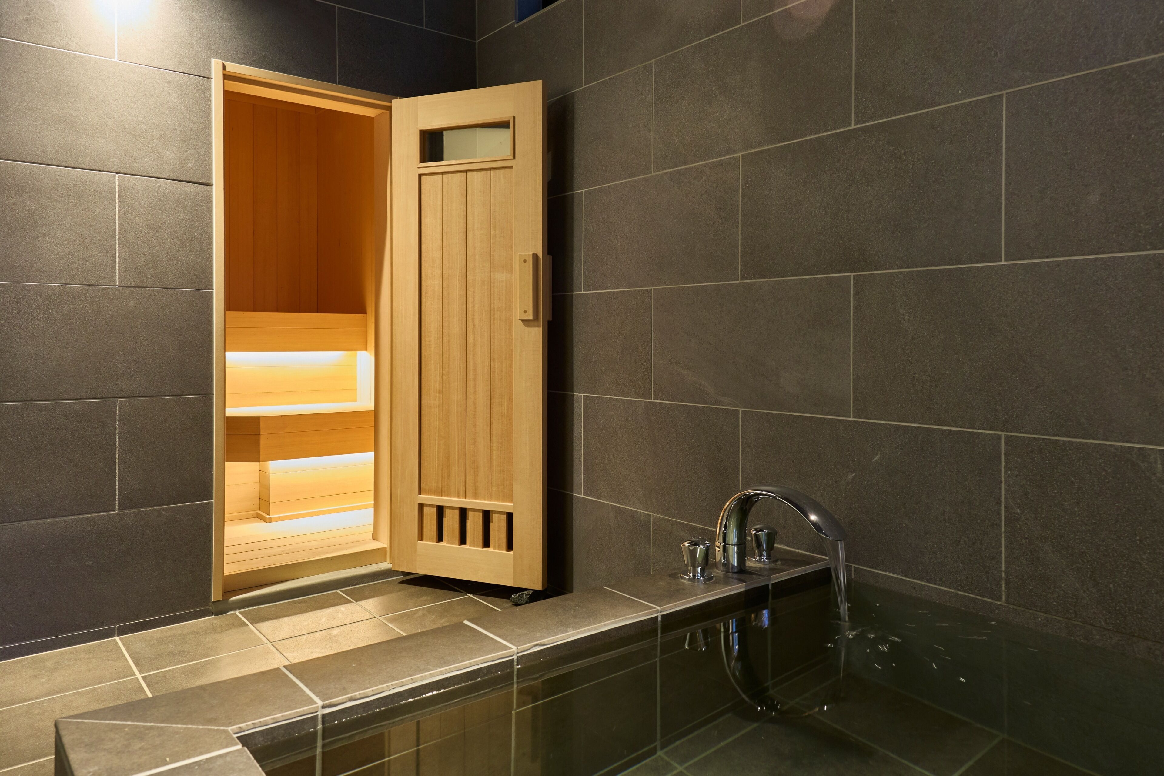 Une salle de bain moderne avec une porte de sauna en bois, une douche à parois de verre et un robinet élégant.