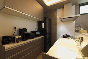 A modern kitchen with a built-in microwave, toaster, and coffee maker, a stainless steel refrigerator, and a white countertop with a sink. - HAKATASUITEI (Fukuoka)