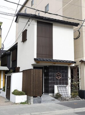 A modern two-story building with a white facade, a wooden slatted entrance, and a black door with a decorative emblem.