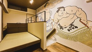 A room with a bed, a wooden headboard, a wall mural of sumo wrestlers, and a staircase.