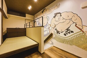 Una habitación con una cama, cabecera de madera, un mural en la pared con luchadores de sumo y una escalera.