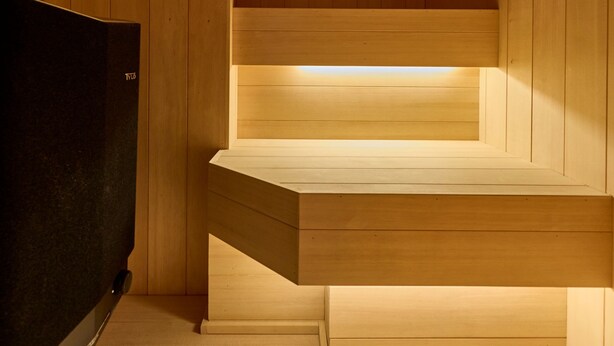 A sauna room with wooden walls and benches, a black heater, and a visible light source.
