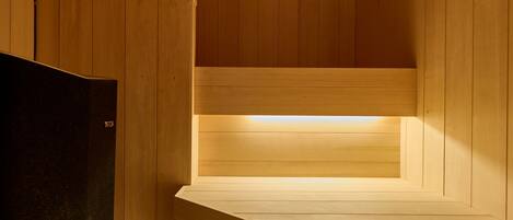 A sauna room with wooden walls and benches, a black heater, and a visible light source.