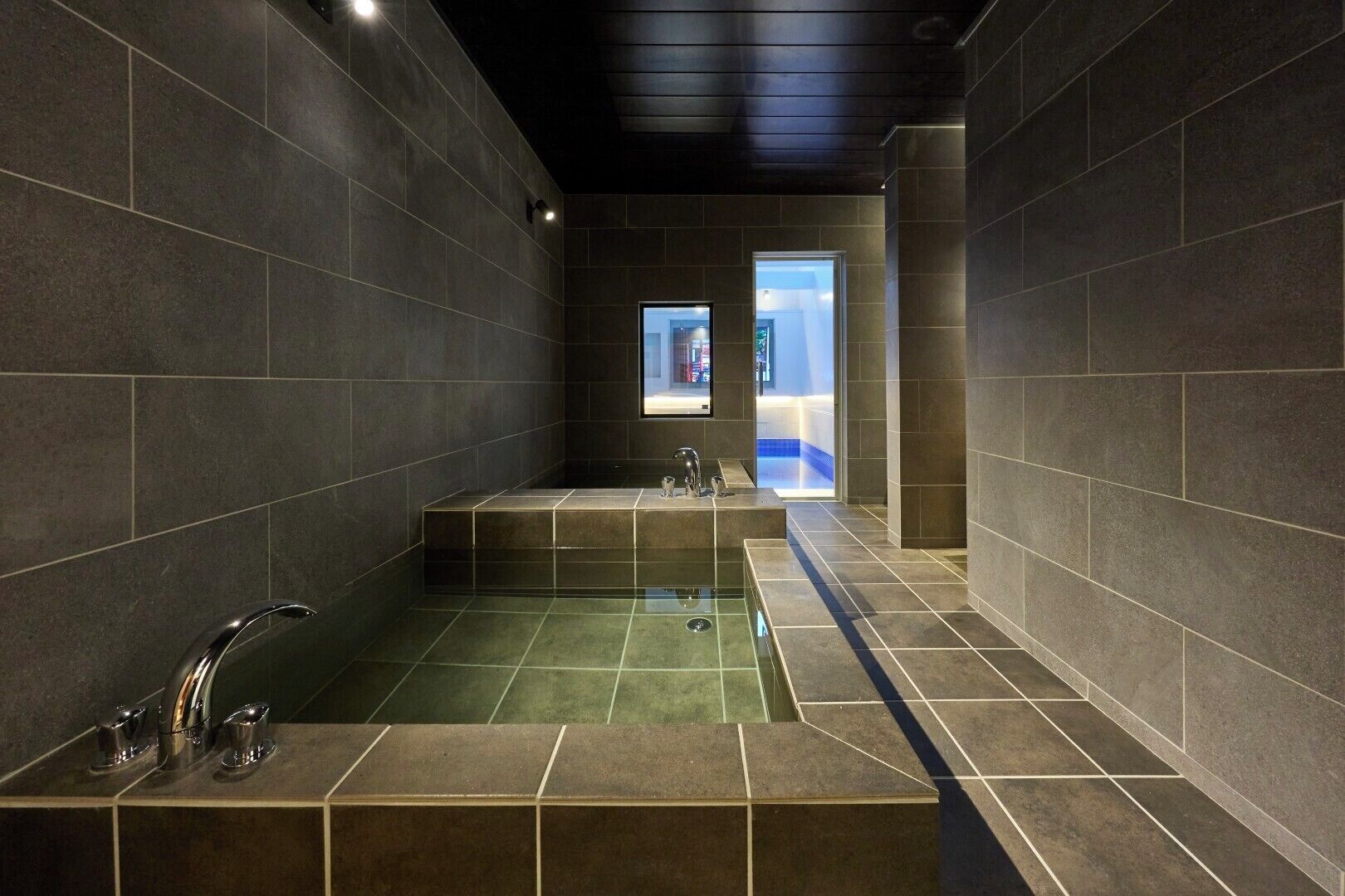 A modern bathroom with dark tiled walls, a central bathtub, and a separate shower area.