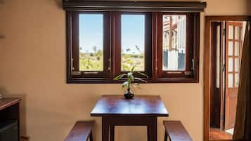 A room with a wooden table, two benches, a window with a view, and a woven ceiling.